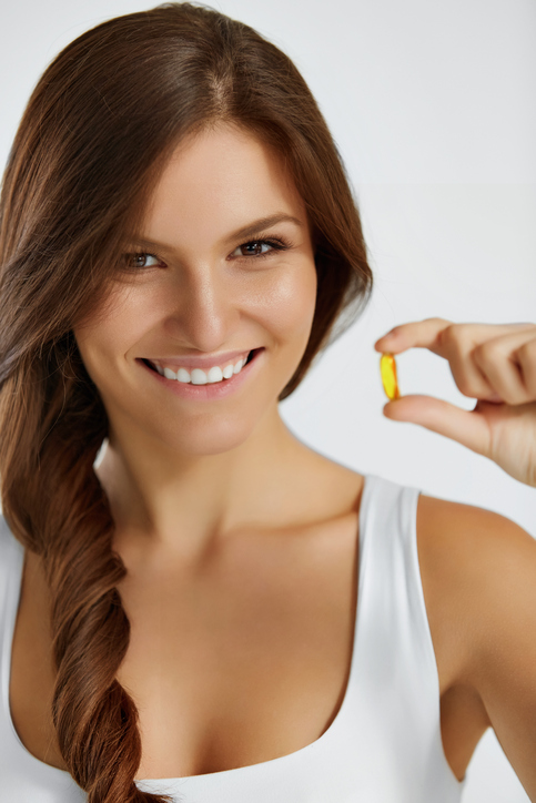 Daily Maintenance & Detoxification. Image: Happy young woman in white is smiling while holding a wheat germ oil supplement. 